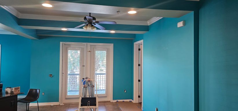 A bright turquoise room with a ceiling fan and double doors leading outside.